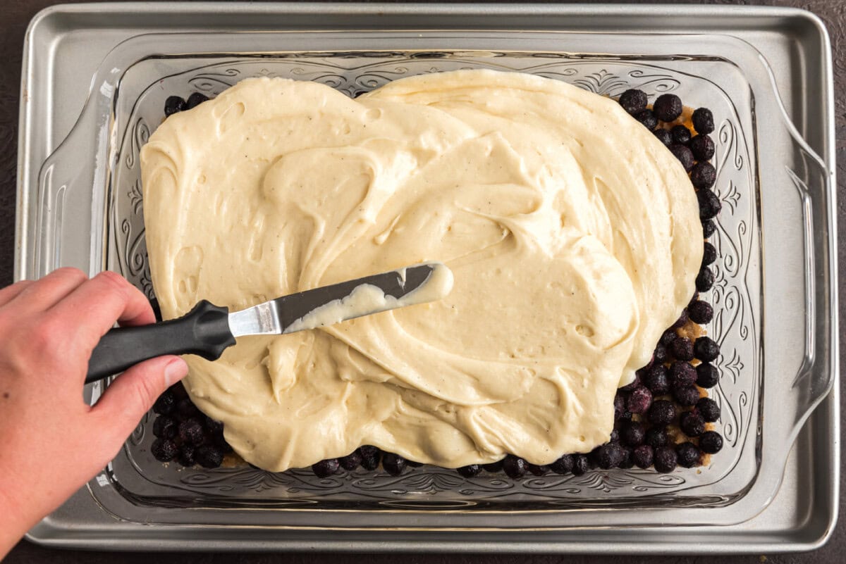 spreading cake batter over blueberries and brown sugar mixture