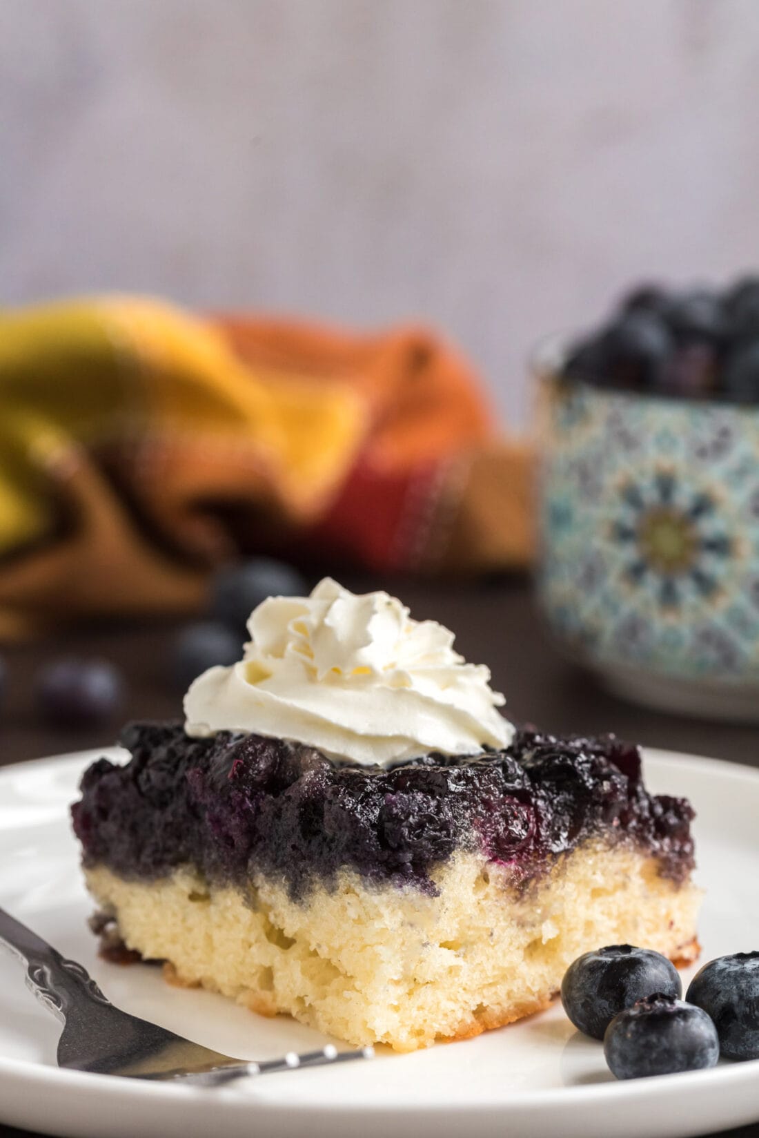 Piece of Easy Blueberry Upside Down Cake on a plate topped with whipped cream