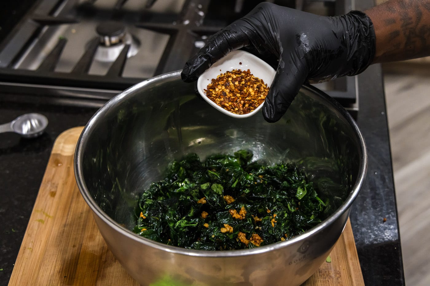 adding red pepper flakes to spinach and garlic