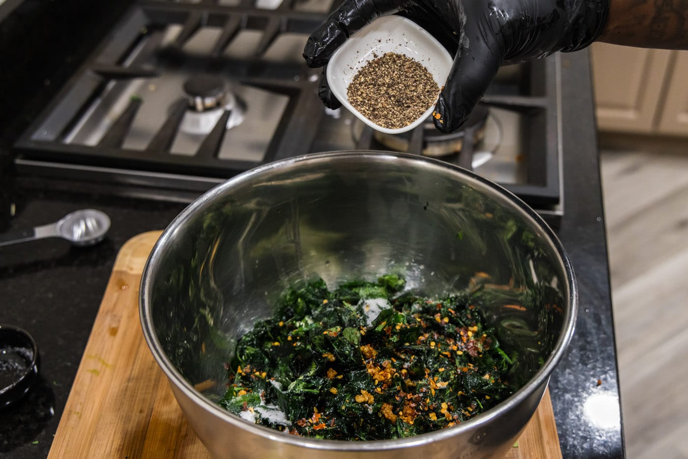 adding black pepper to fried spinach with red pepper flakes and garlic