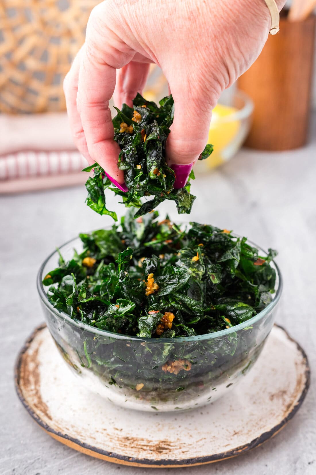 A hand grabbing Fried Spinach out of a bowl