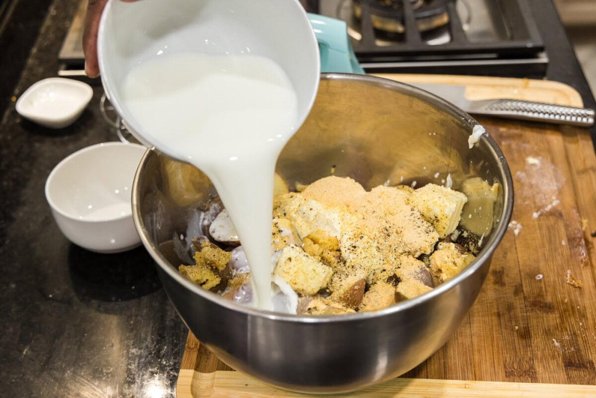 pouring heavy whipping cream into bowl of sour cream, butter, potatoes, and garlic