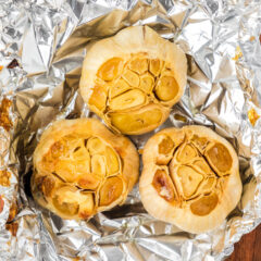 Close up photo of three bulbs of roasted garlic in foil