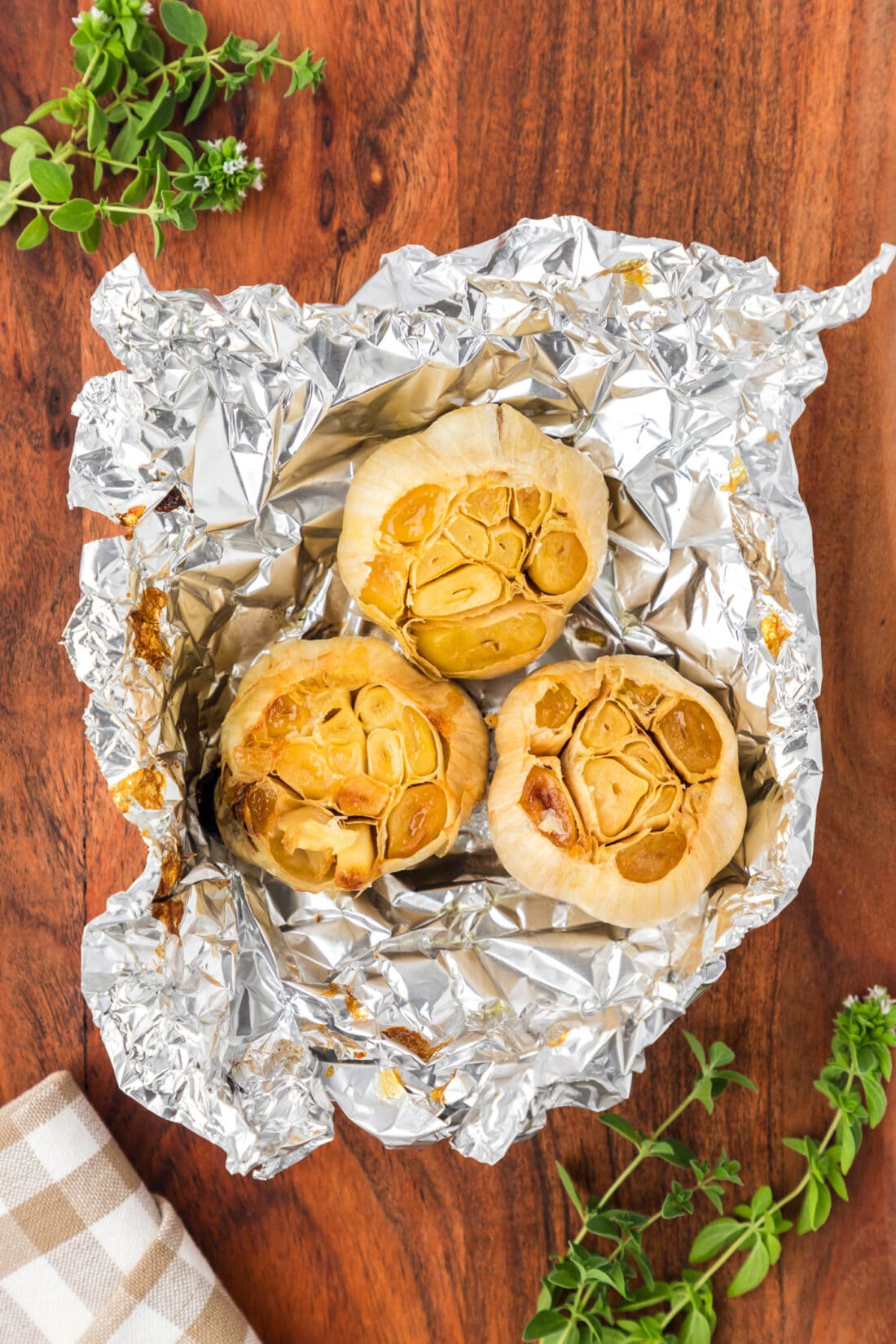 Three bulbs of roasted garlic in foil on a wooden board