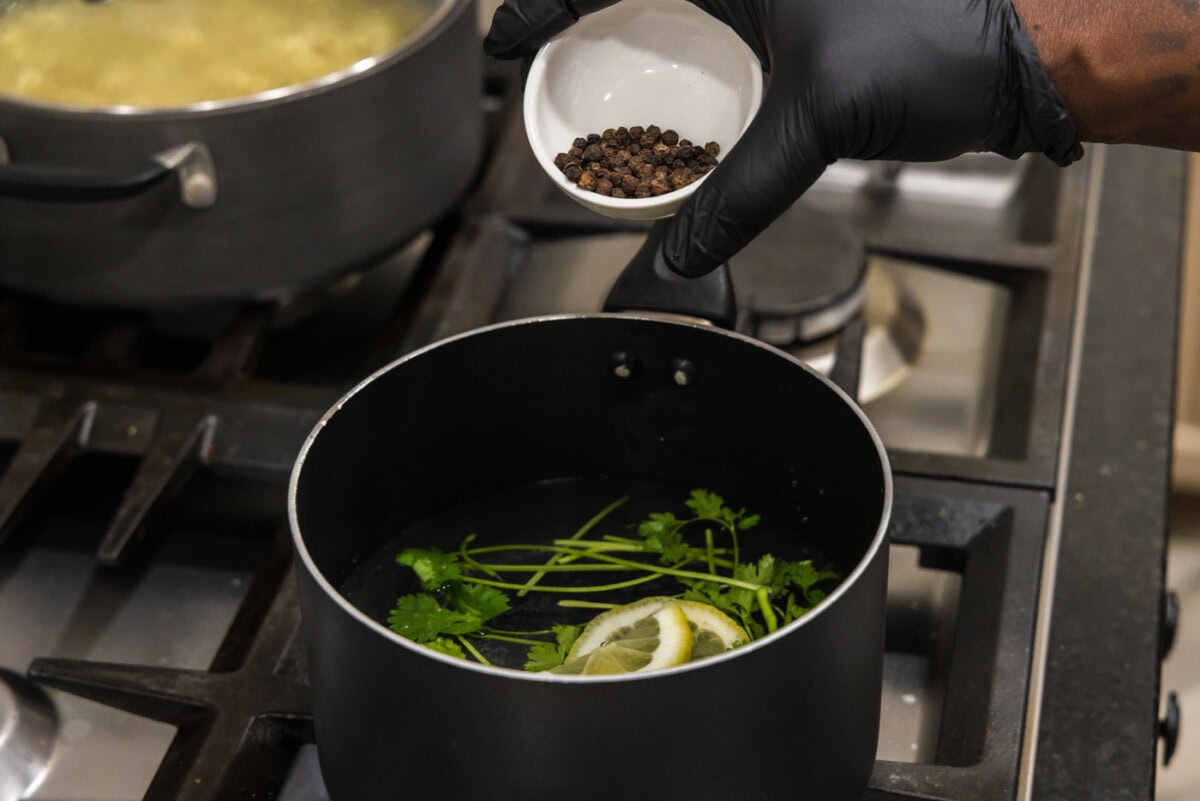 adding black peppercorns to pot of cilantro, lemons, and garlic salt