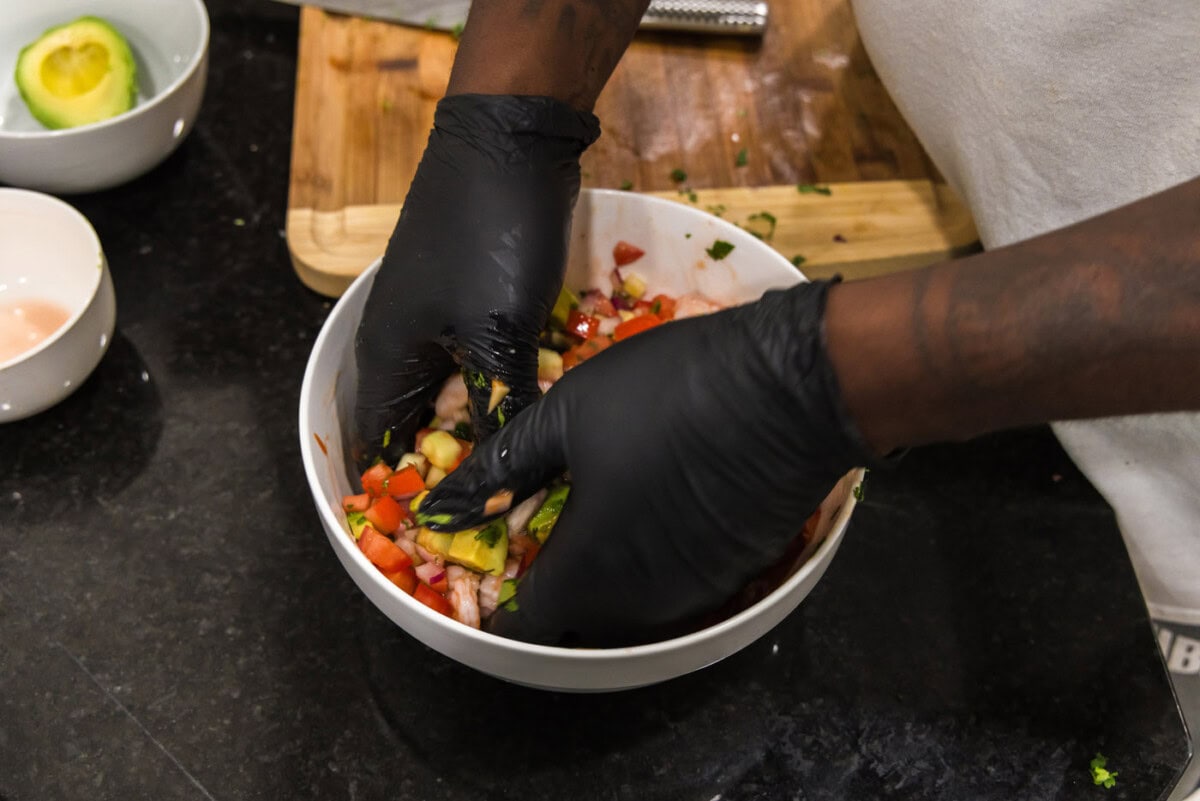 hands tossing mexican shrimp cocktail in a bowl