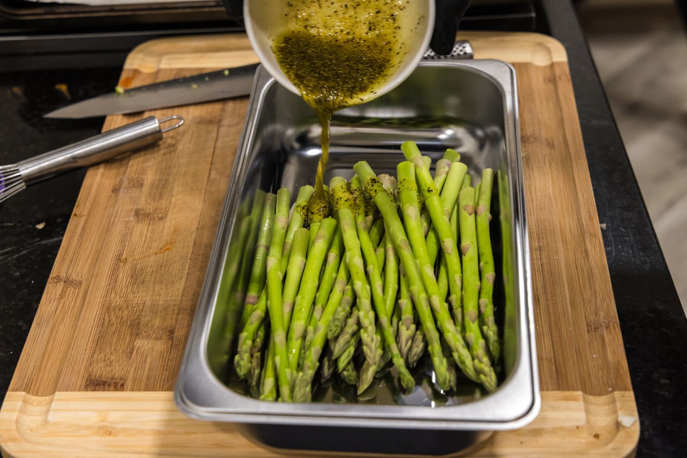 pouring olive oil seasoning mixture over asparagus spears