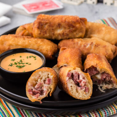 Close up photo of a Reuben Egg Roll cut in half on a plate with more rolls in the background