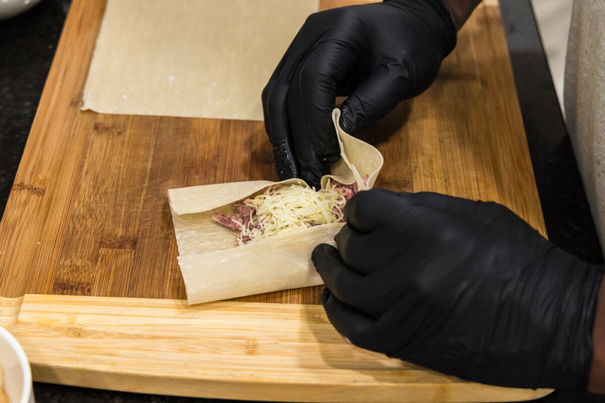 hands folding an egg roll wrapper with corned beef and swiss cheese