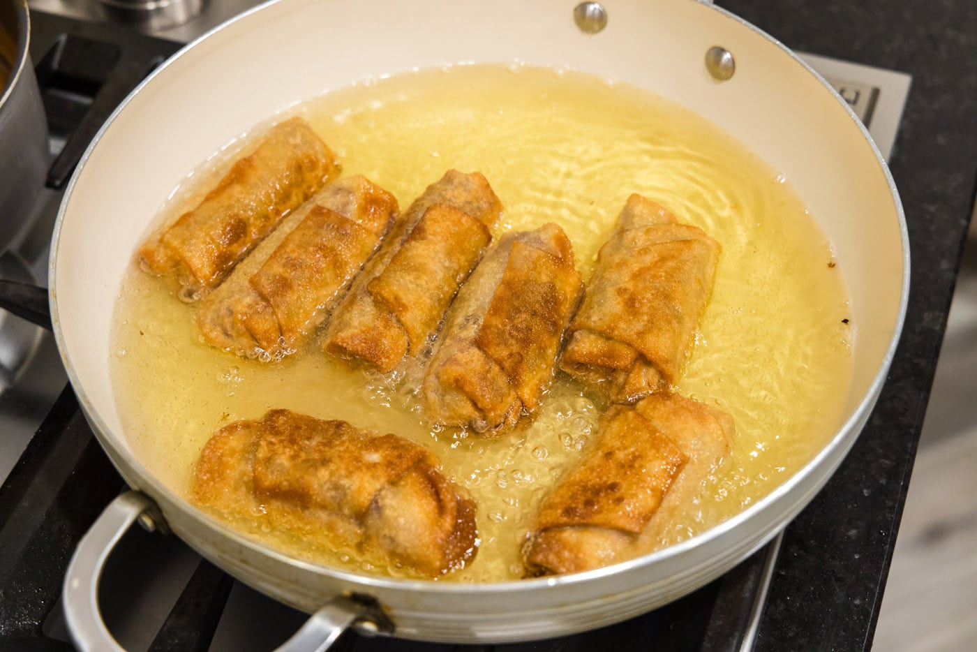 golden fried reuben egg rolls in a skillet of oil