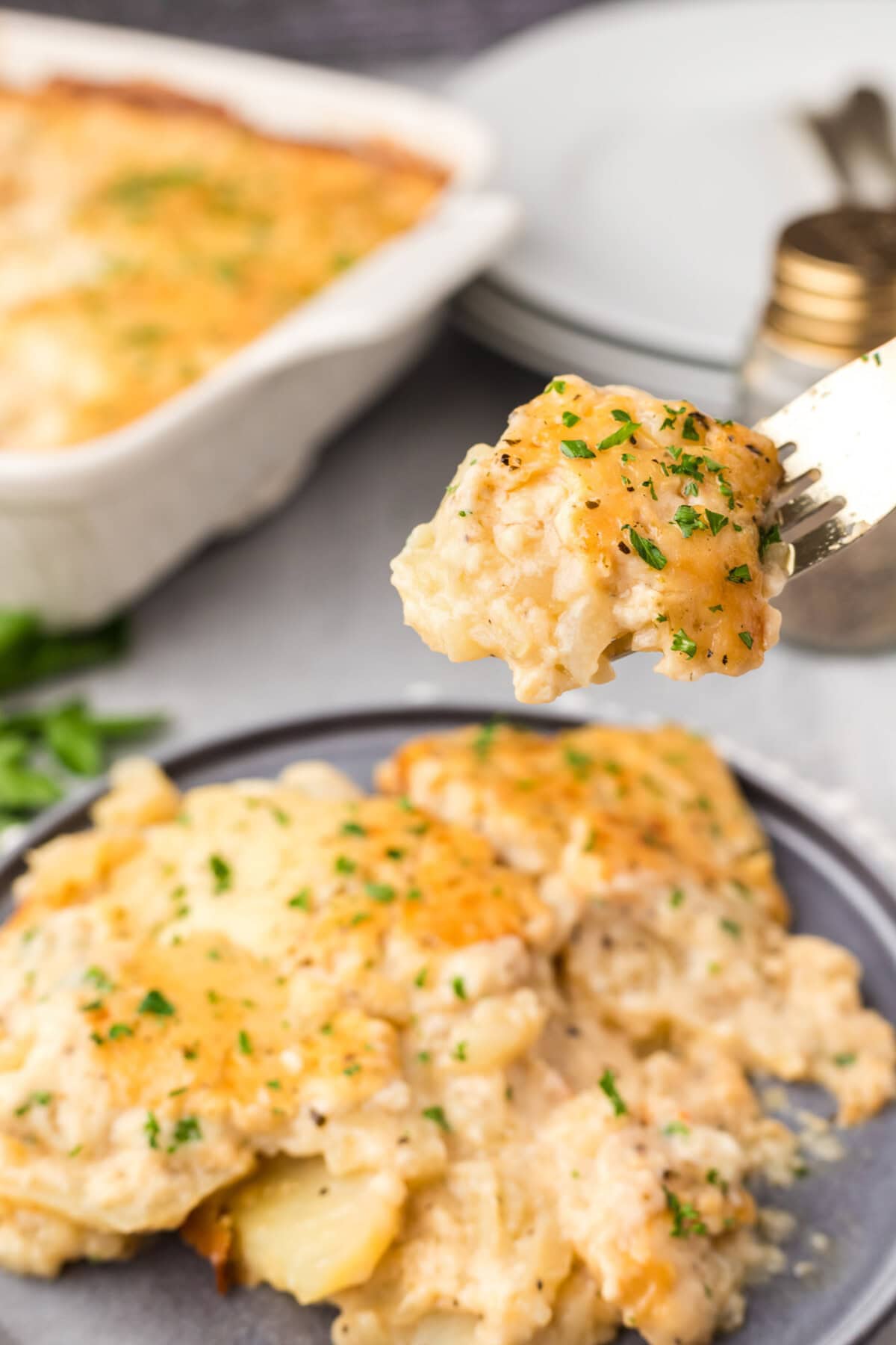 Scalloped Potatoes on a fork held above a plate of Scalloped Potatoes
