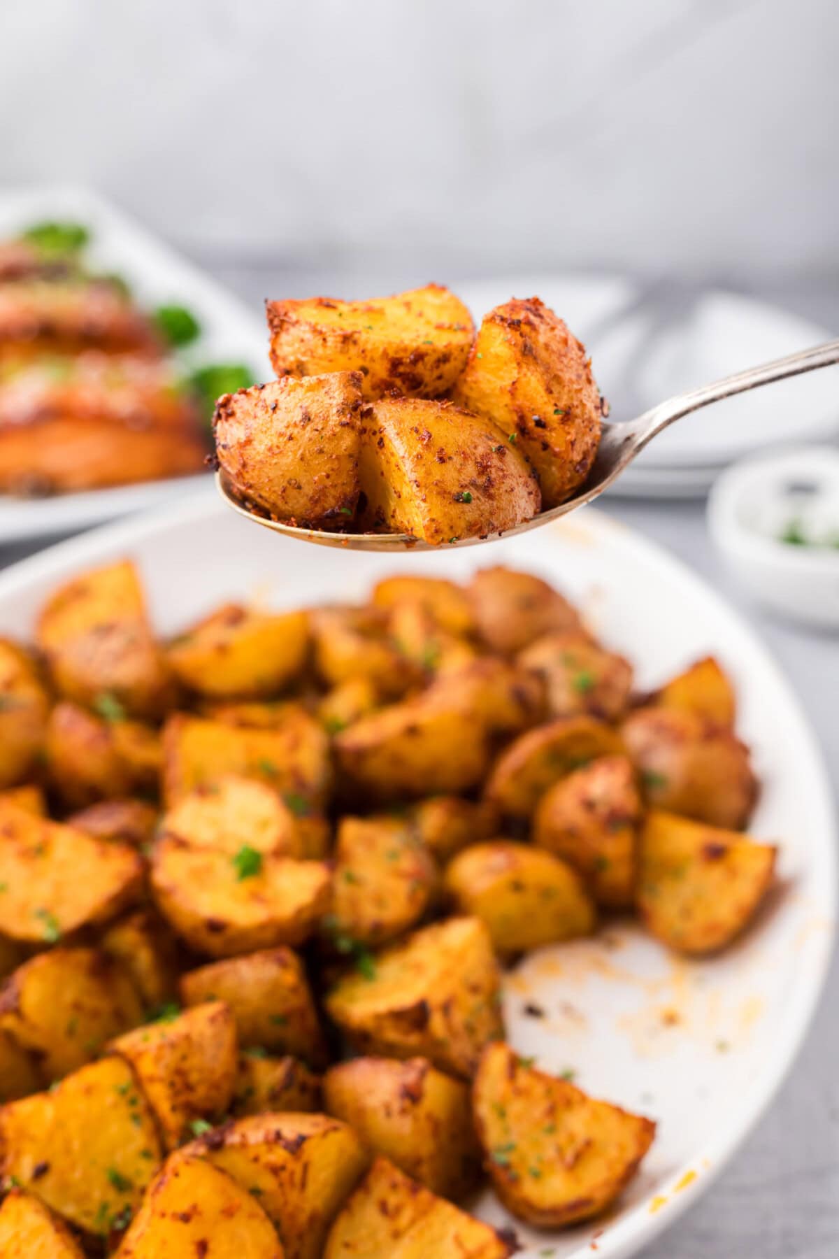 Spoonful of Spicy Potatoes held above a platter of Spicy Potatoes