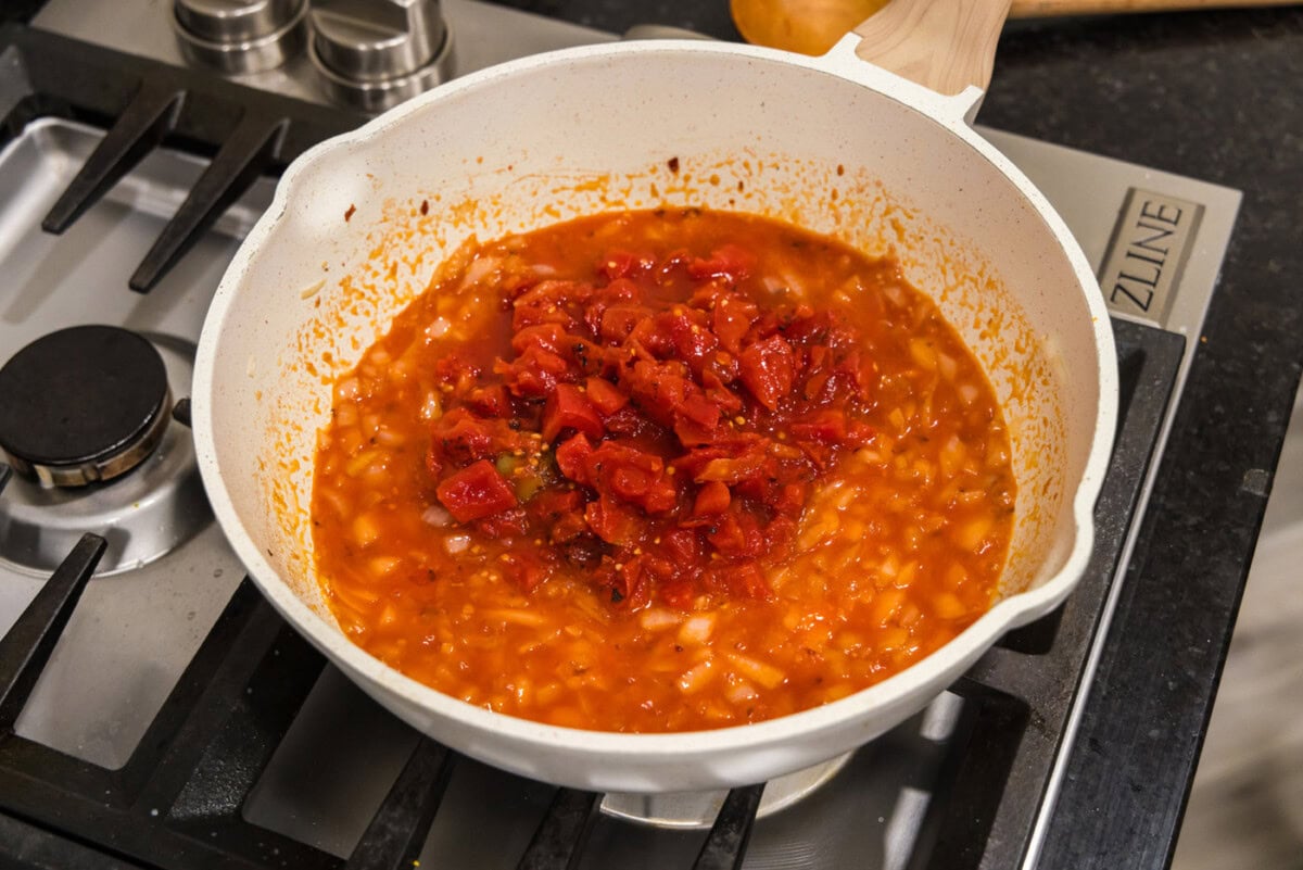adding crushed tomatoes to skillet with vodka and onion mixture