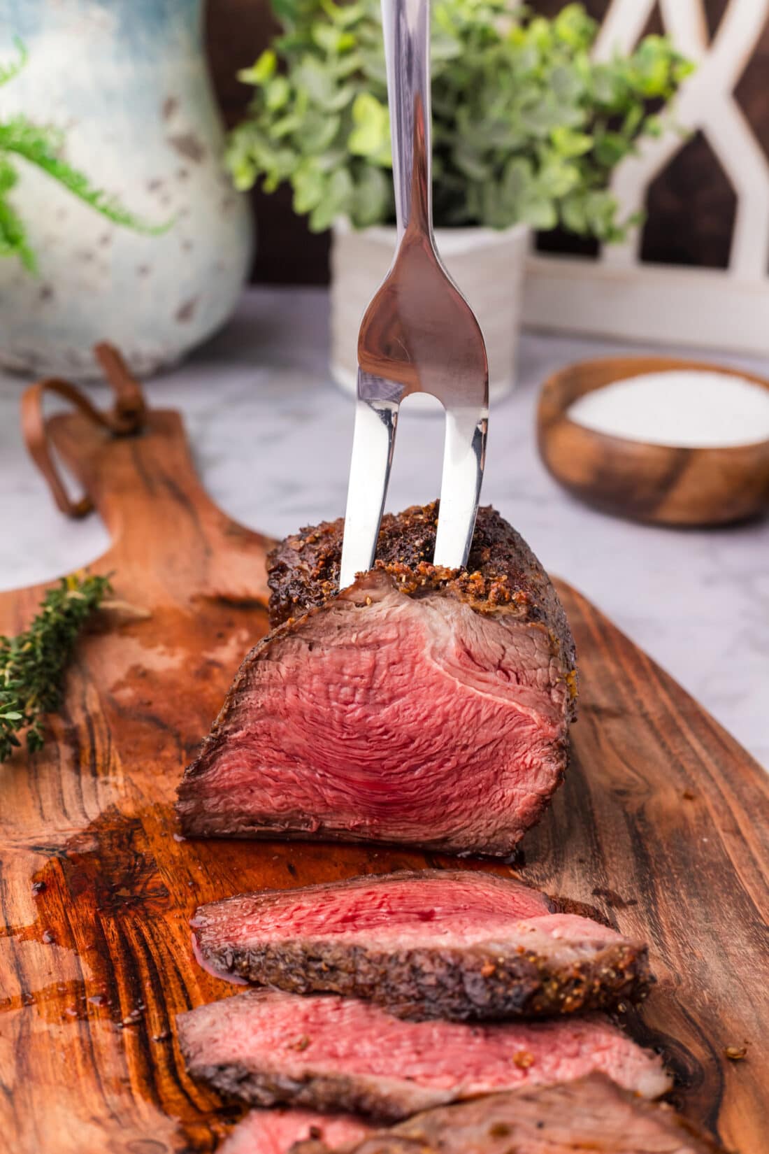 Carving fork holding an Air Fryer Roast Beef on a wooden board