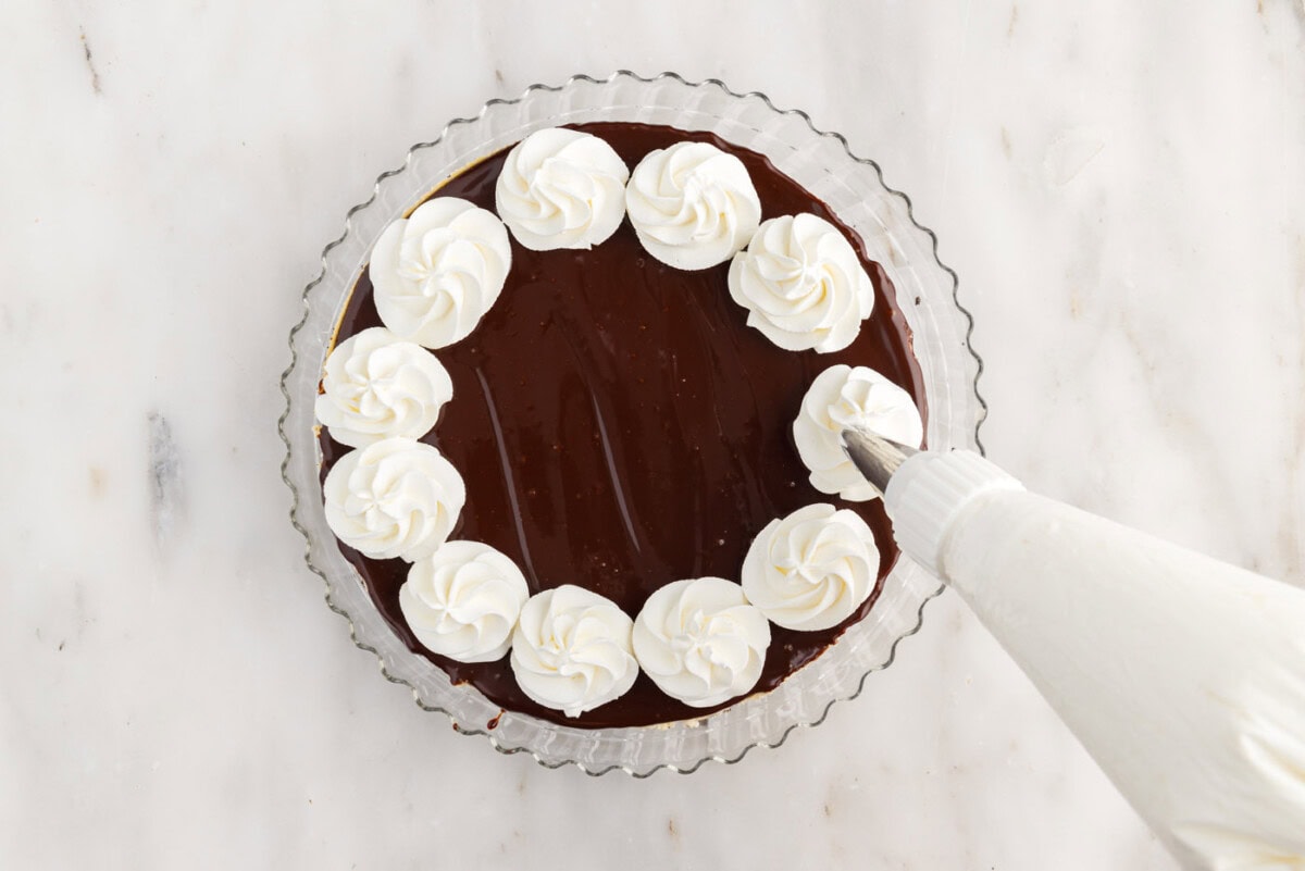 piping whipped cream onto cheesecake