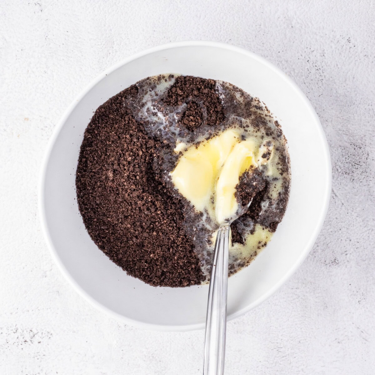 mixing melted butter with crushed oreo cookies