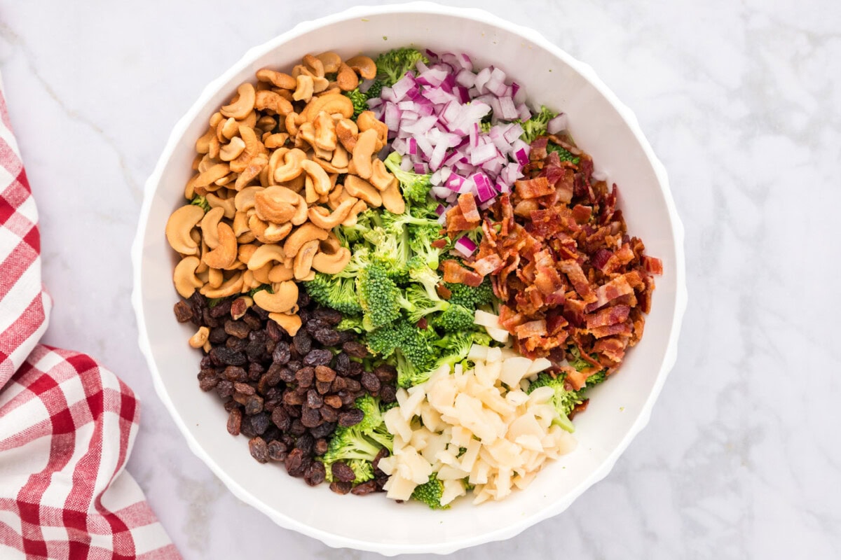 bacon, raisins, cashews, water chestnuts, and onion with broccoli in a bowl