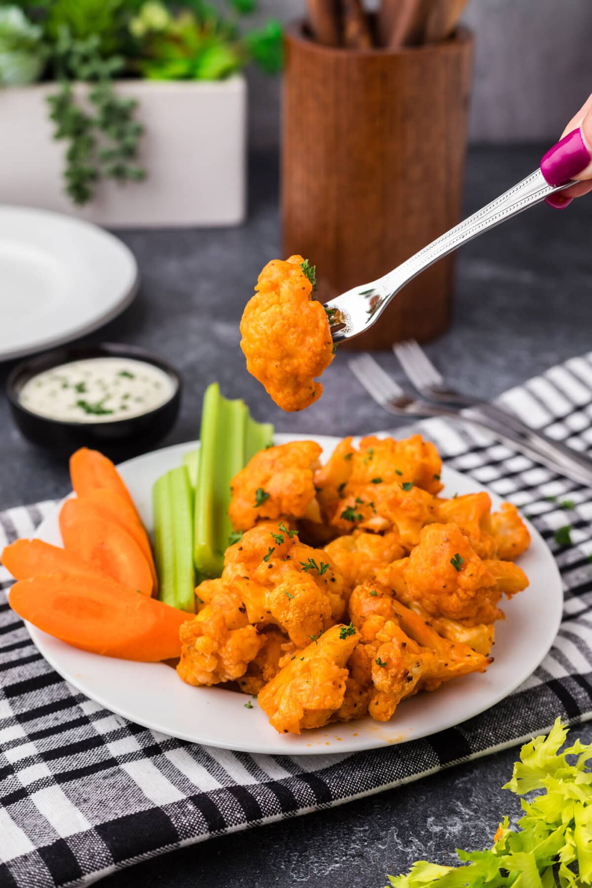 Buffalo Cauliflower on a fork held above a plate of Buffalo Cauliflower