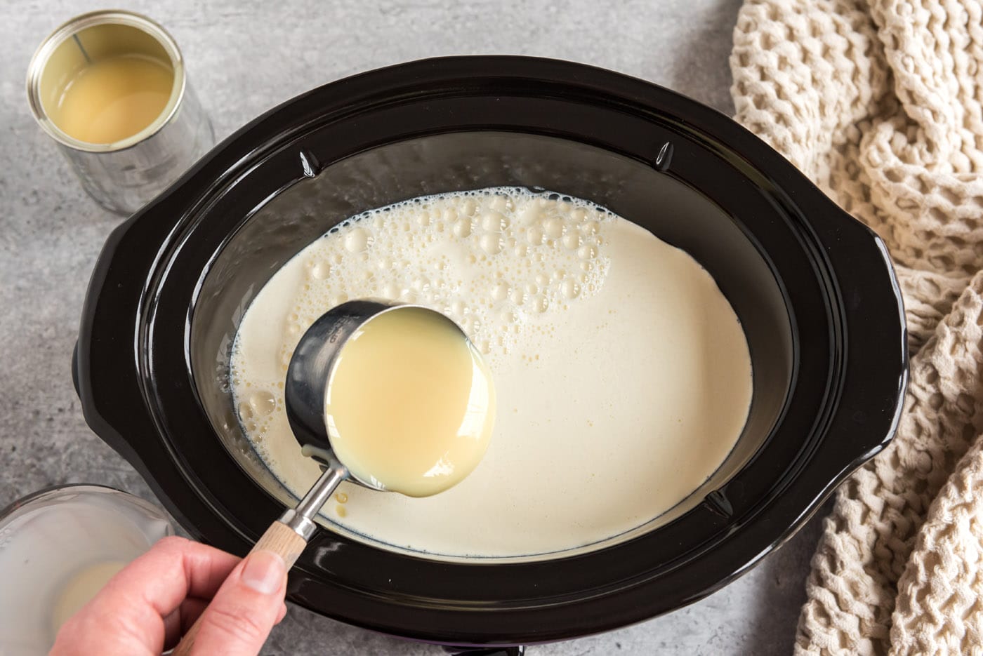 pouring sweetened condensed milk into crockpot with heavy whipping cream