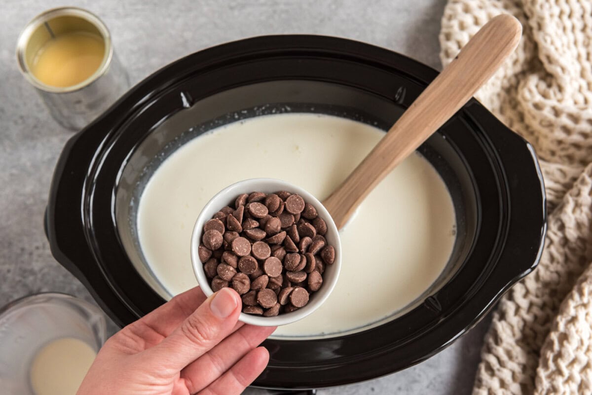 adding chocolate chips to crockpot with heavy cream and sweetened condensed milk