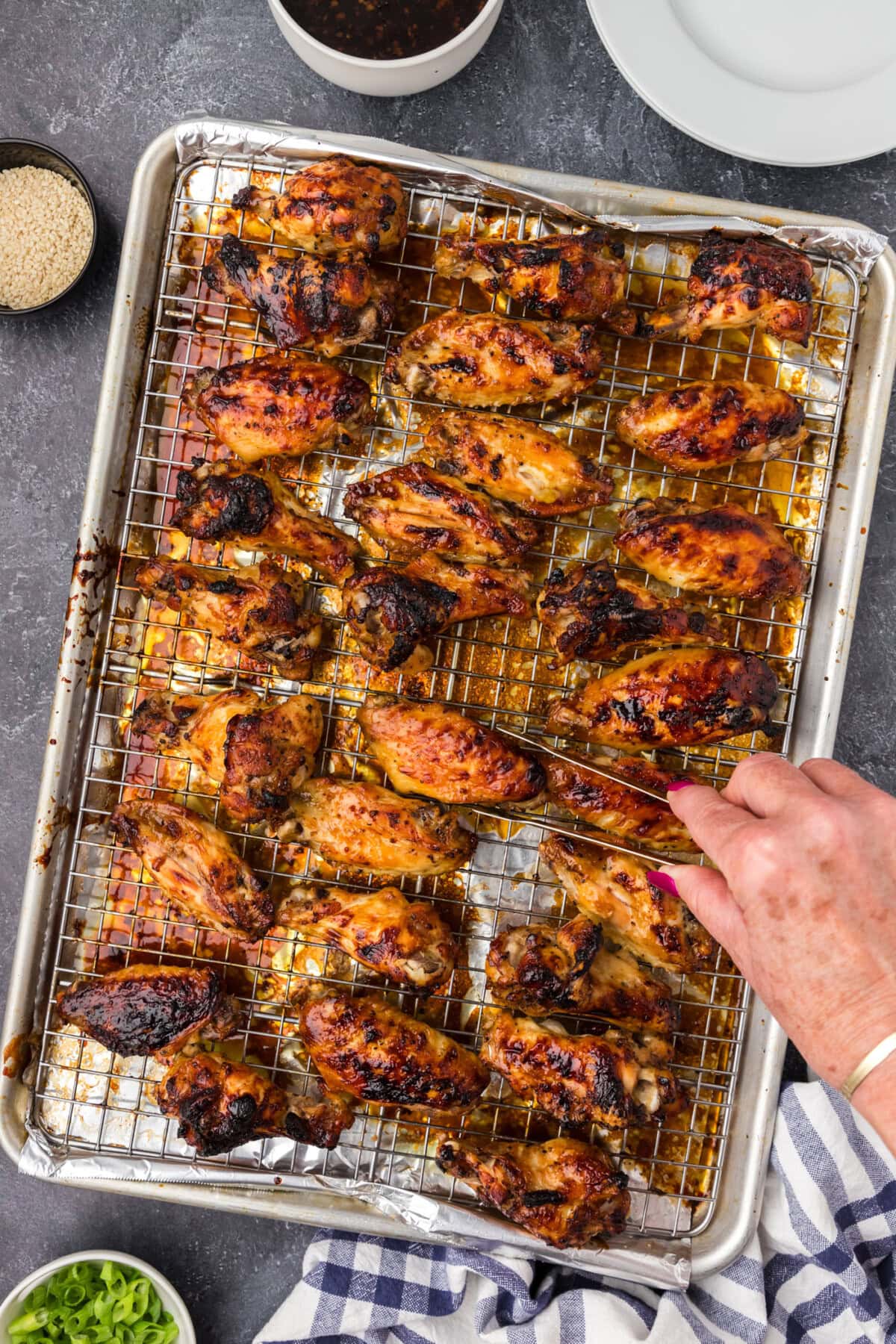 Hand grabbing a Honey Garlic Chicken Wing off a sheet pan of Honey Garlic Chicken Wings