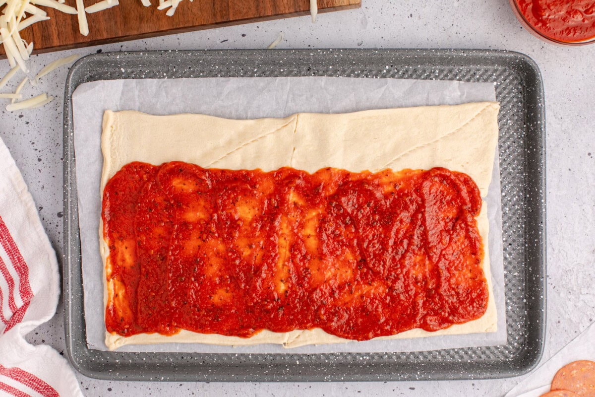 pizza sauce spread on top of crescent roll dough