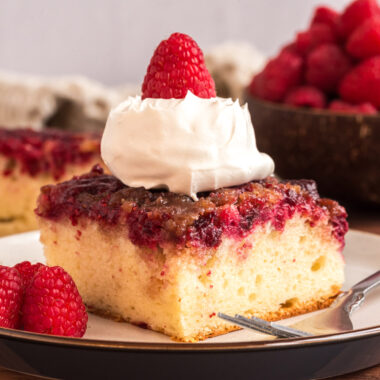 Close up photo of Raspberry Upside Down Cake on a platted topped with whipped cream and a raspberry