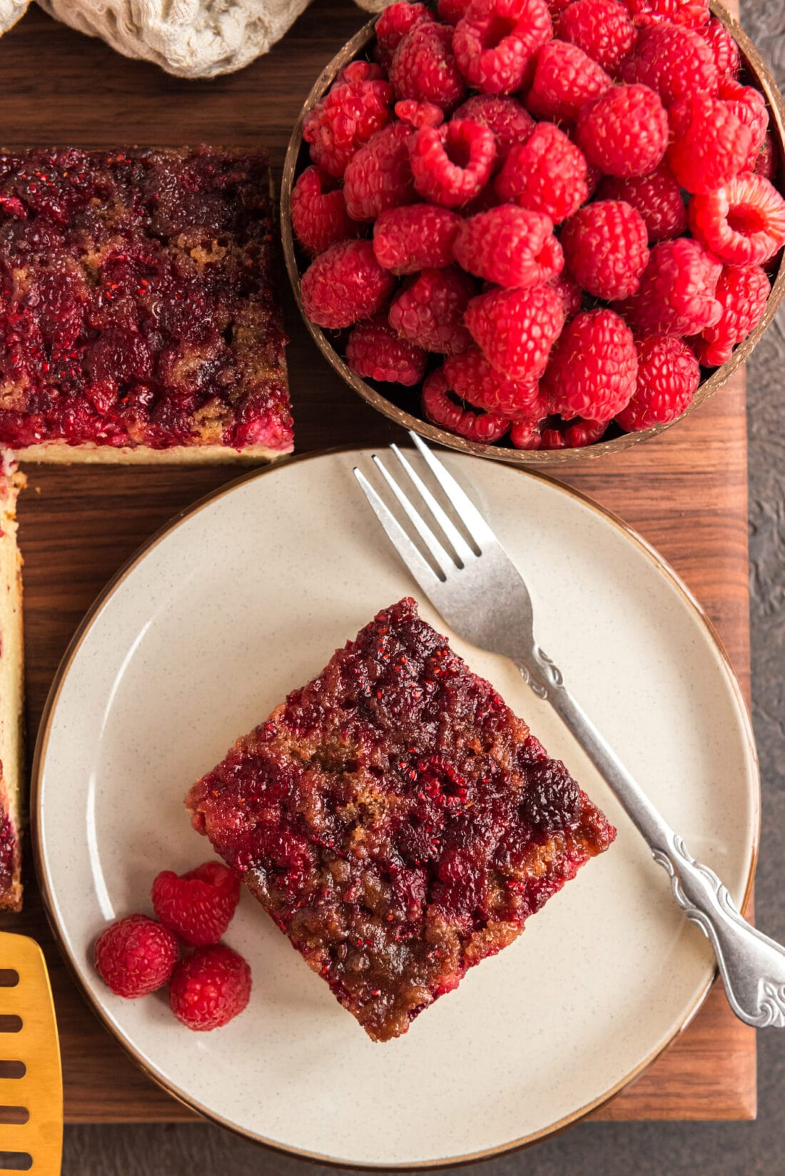 Square of Raspberry Upside Down Cake on a plate with a bowl of raspberries next to it