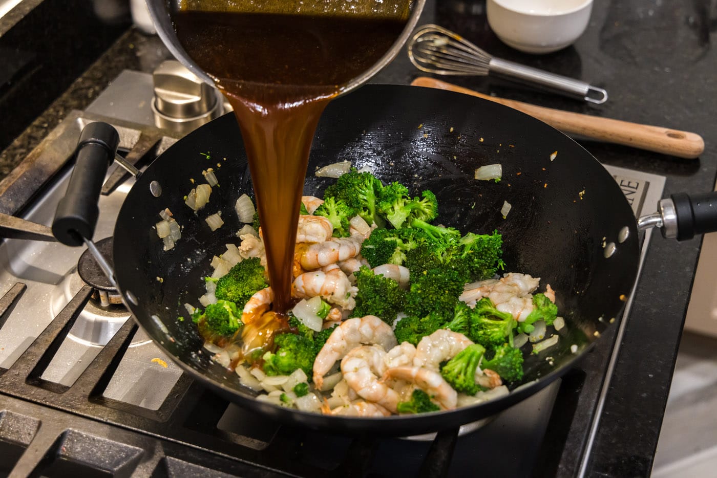 pouring sauce over shrimp and broccoli in a wok
