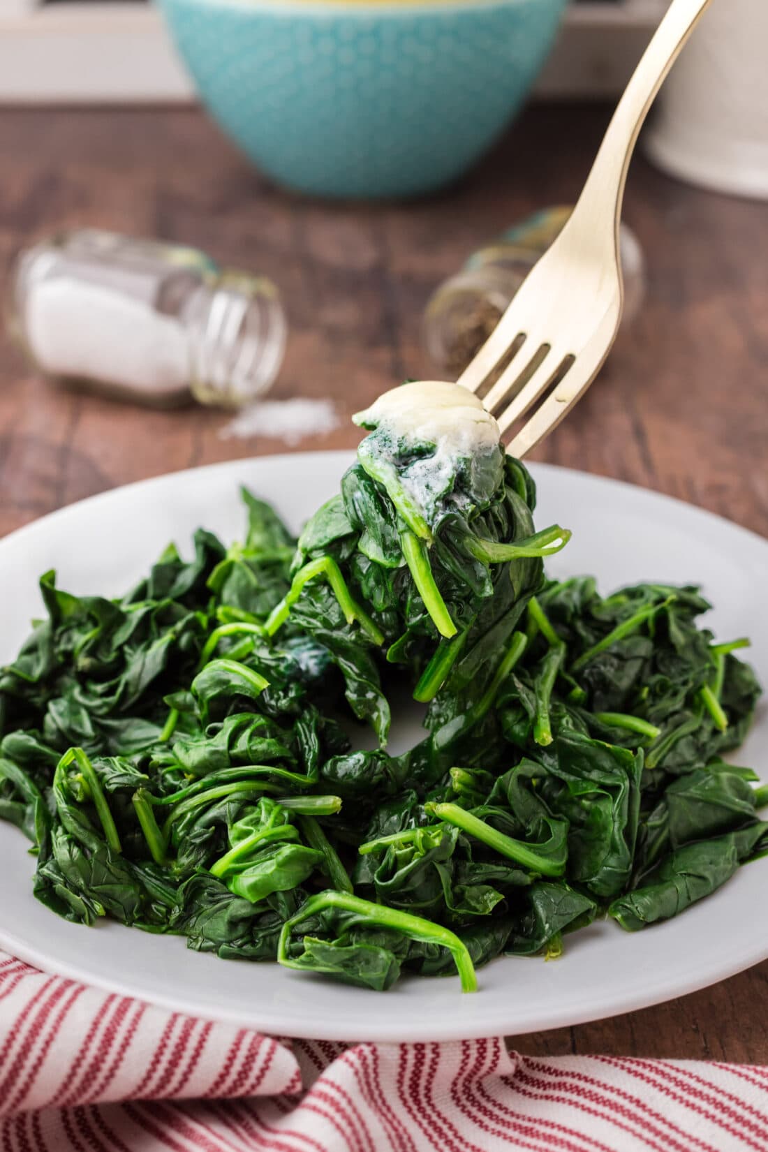 Steamed Spinach being lifted off of a plate by a fork