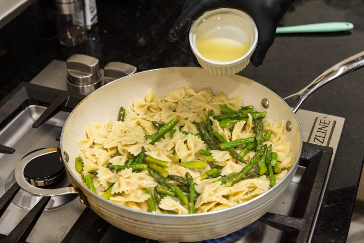 pouring lemon juice over asparagus pasta