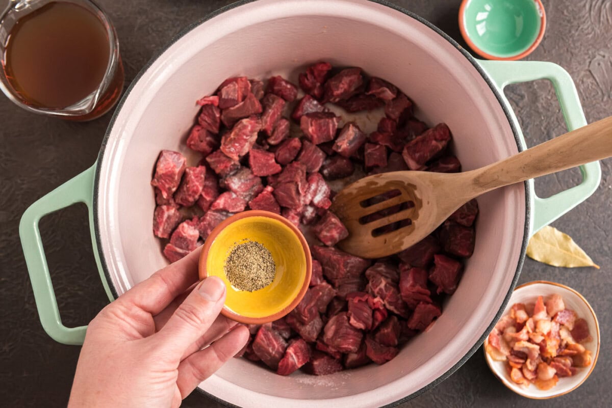 adding seasonings to cubed chuck roast in a dutch oven