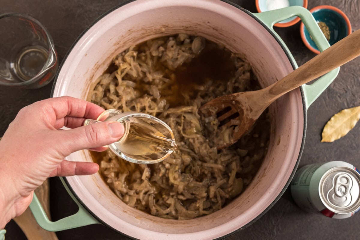 pouring white wine vinegar into pot with onion mixture