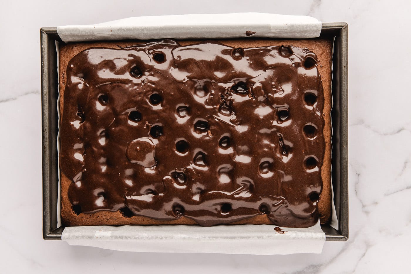 fudge sauce poured over holes in chocolate cake