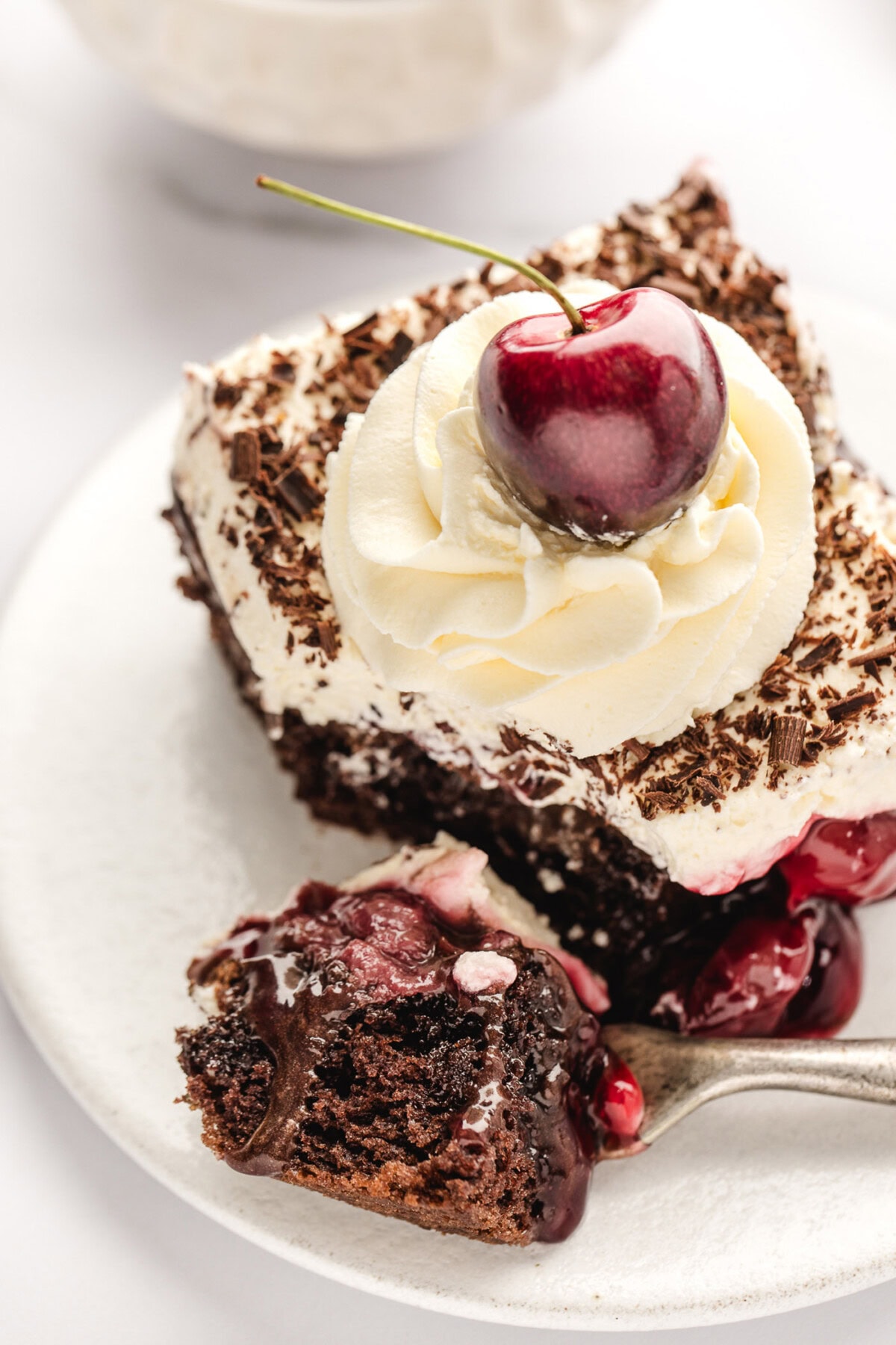 Piece of Black Forest Poke Cake on a plate with a bite removed on a fork