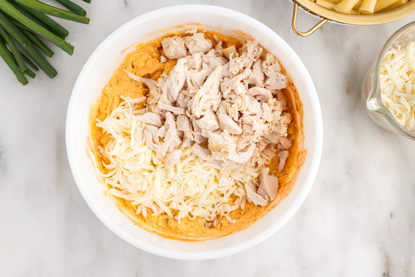 adding shredded cheese and chicken to buffalo chicken mixture
