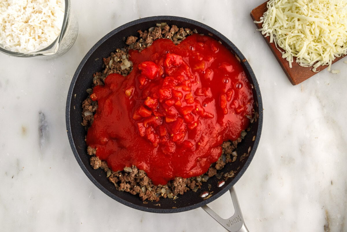 tomato sauce and diced tomatoes added on top of ground beef mixture in skillet