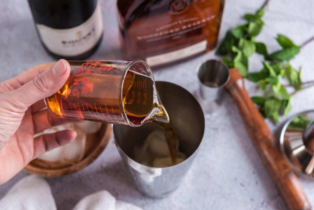 pouring bourbon into cocktail shaker with mint and ice