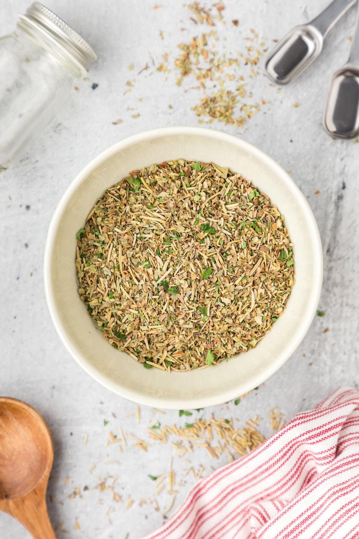 Bowl of Italian Seasoning with measuring spoons and seasoning jar beside it