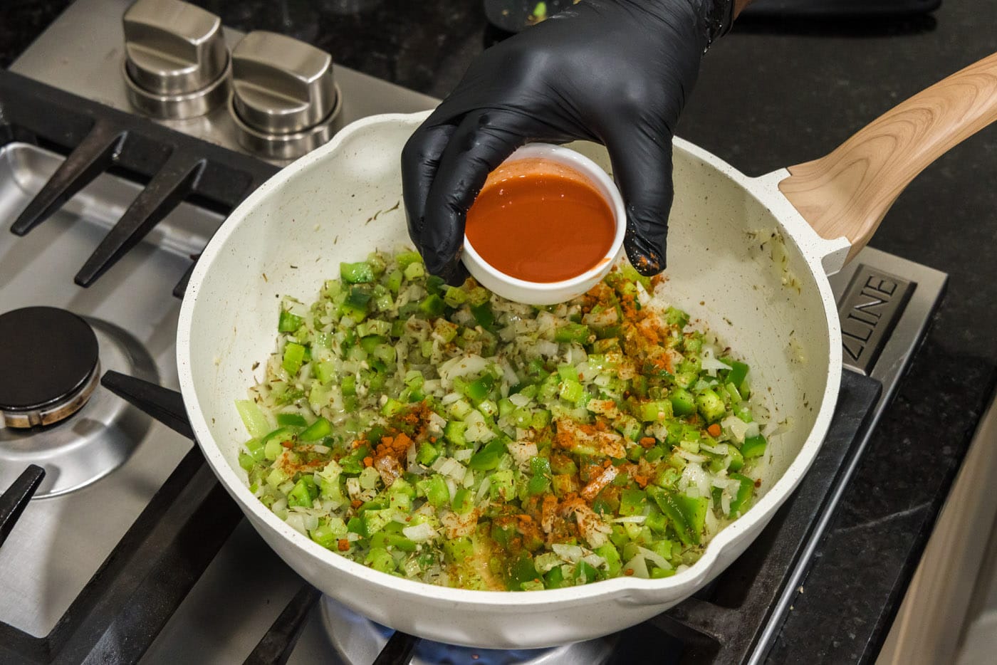 pouring hot sauce and spices into skillet of green pepper, onion, and celery