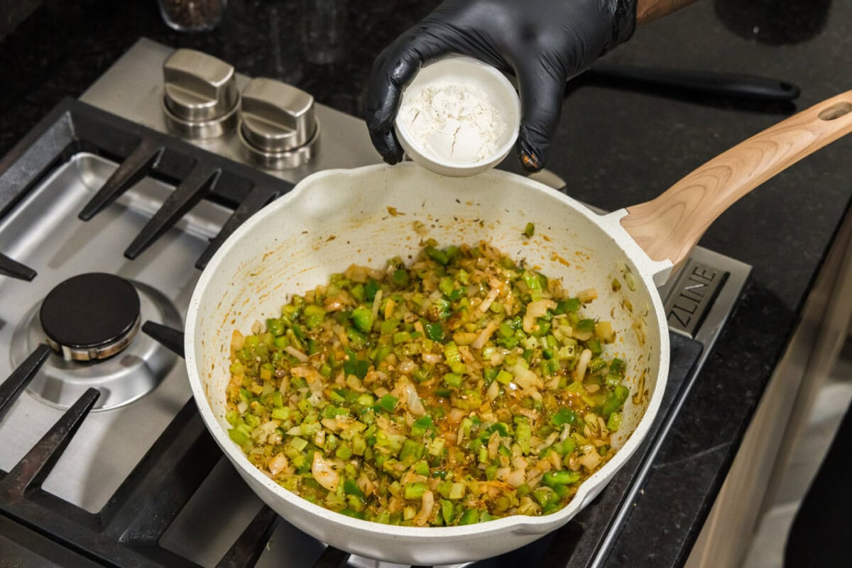 adding flour to skillet of cajun holy trinity and spices