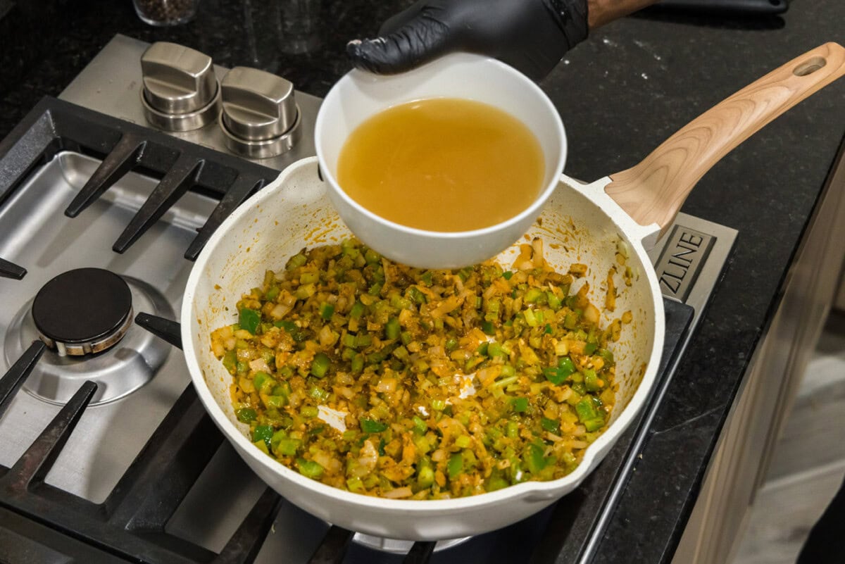 pouring chicken stock into skillet of shrimp creole