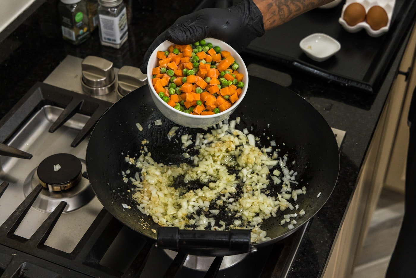 adding frozen peas and carrots to a wok with onion and garlic