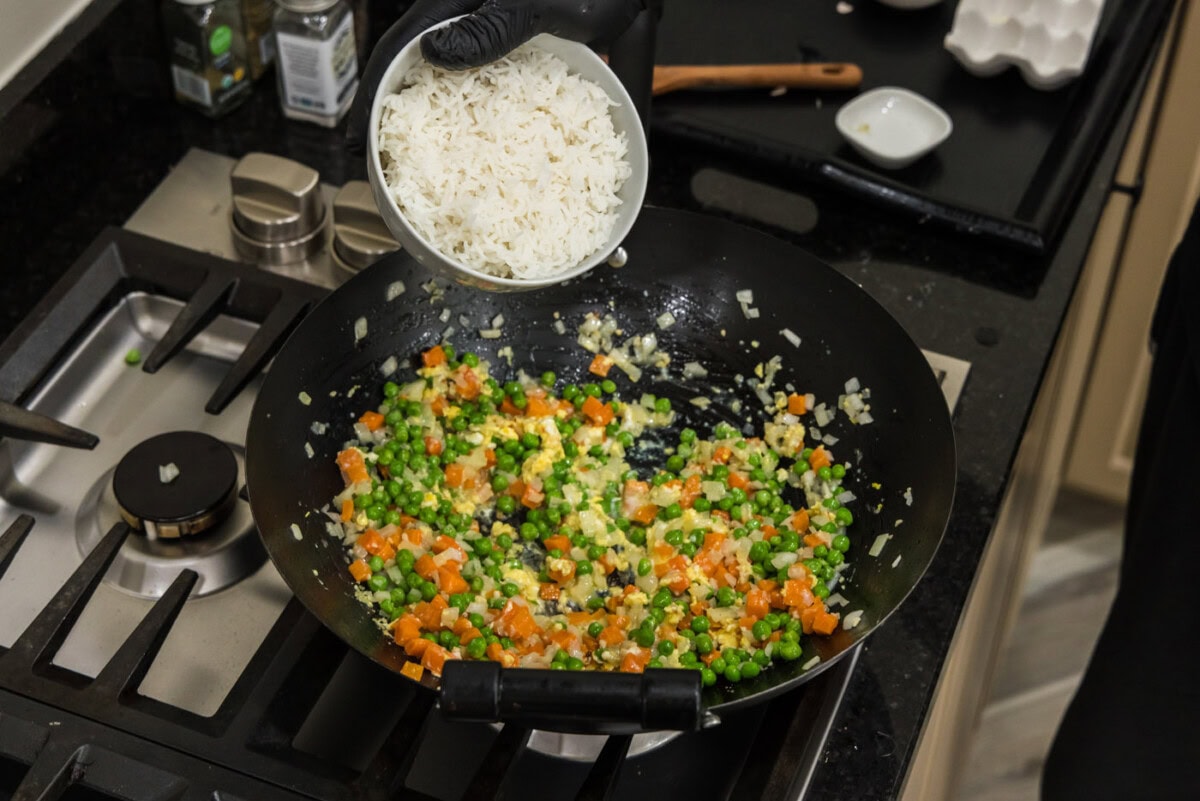 adding cooked rice to wok with vegetables