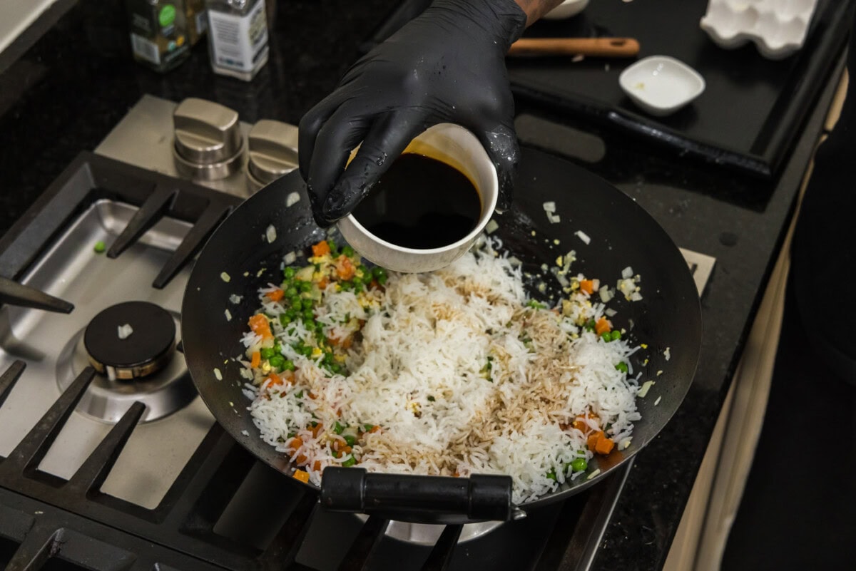 pouring soy sauce into wok with rice and vegetables
