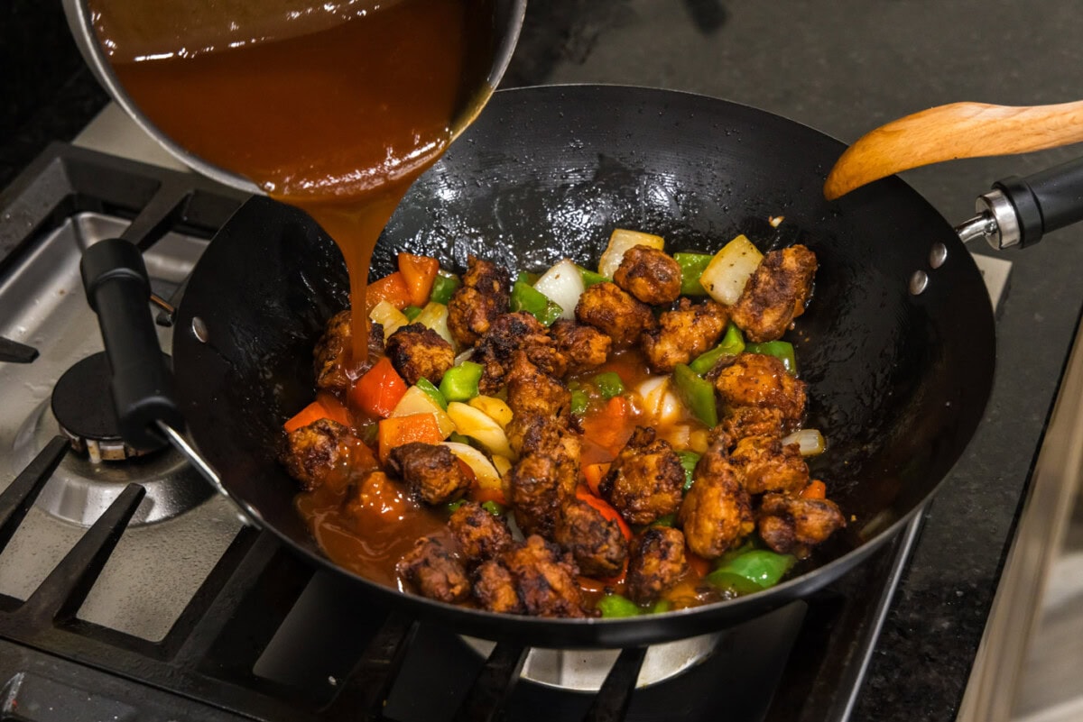 pouring sweet and sour sauce over chicken and stir fried veggies