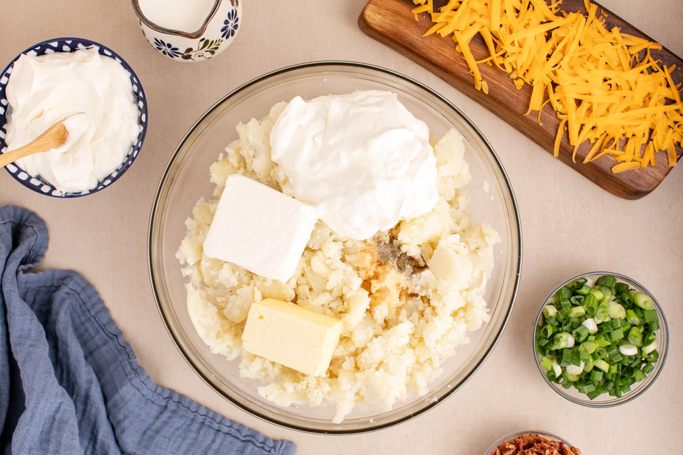 sour cream, cream cheese, milk, butter, and seasonings added to potatoes in a bowl