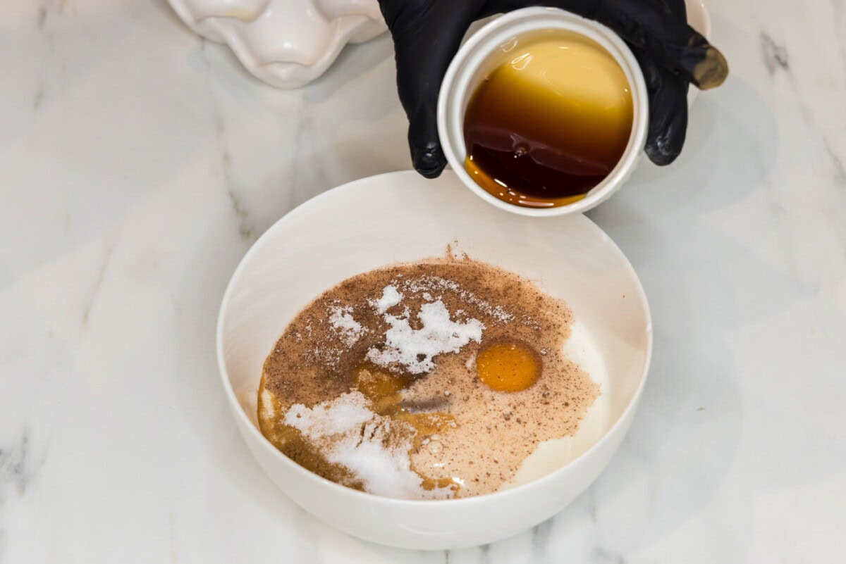 hand pouring maple syrup into French toast batter in a bowl