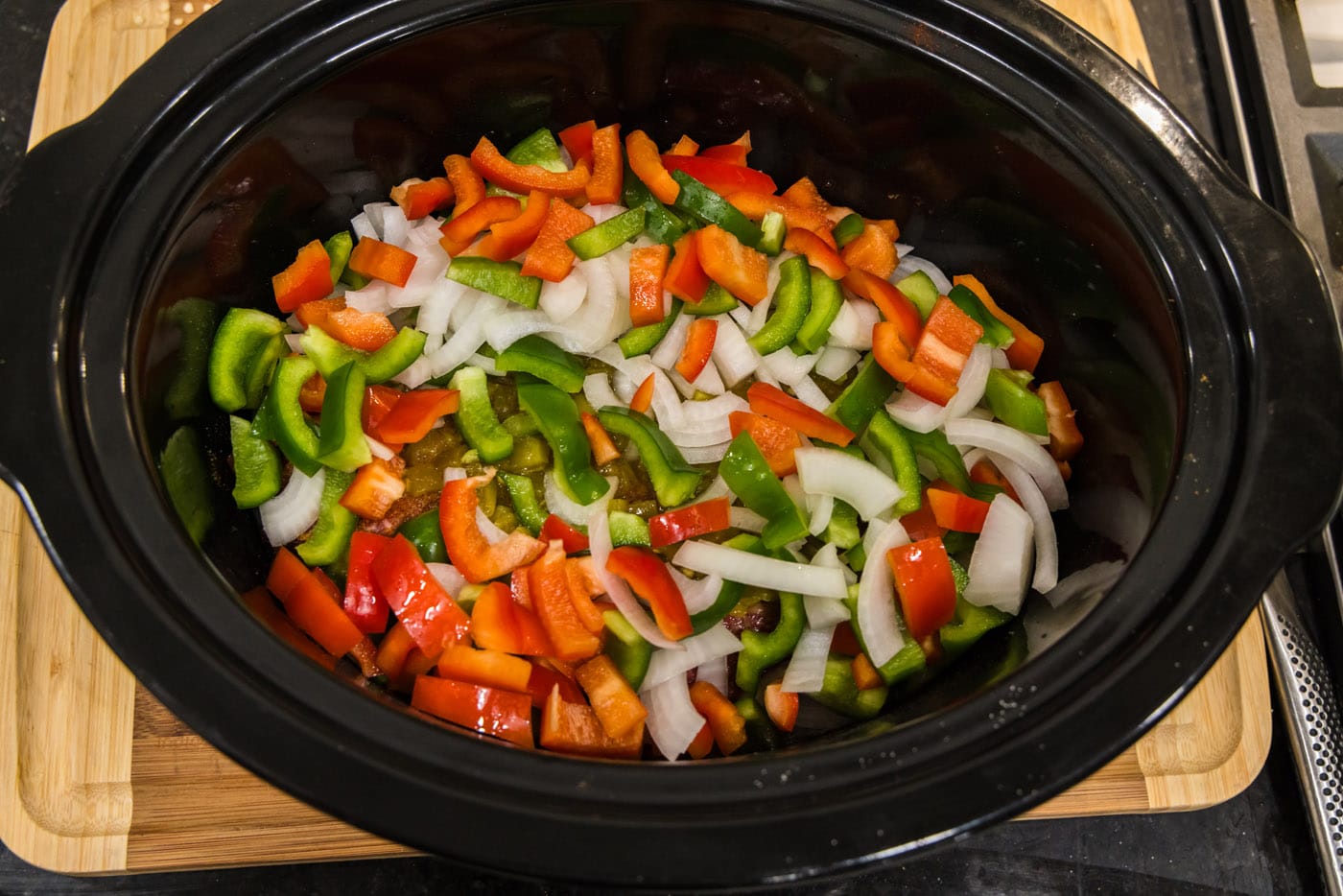 chopped bell peppers and onions on top of chuck roast in crockpot