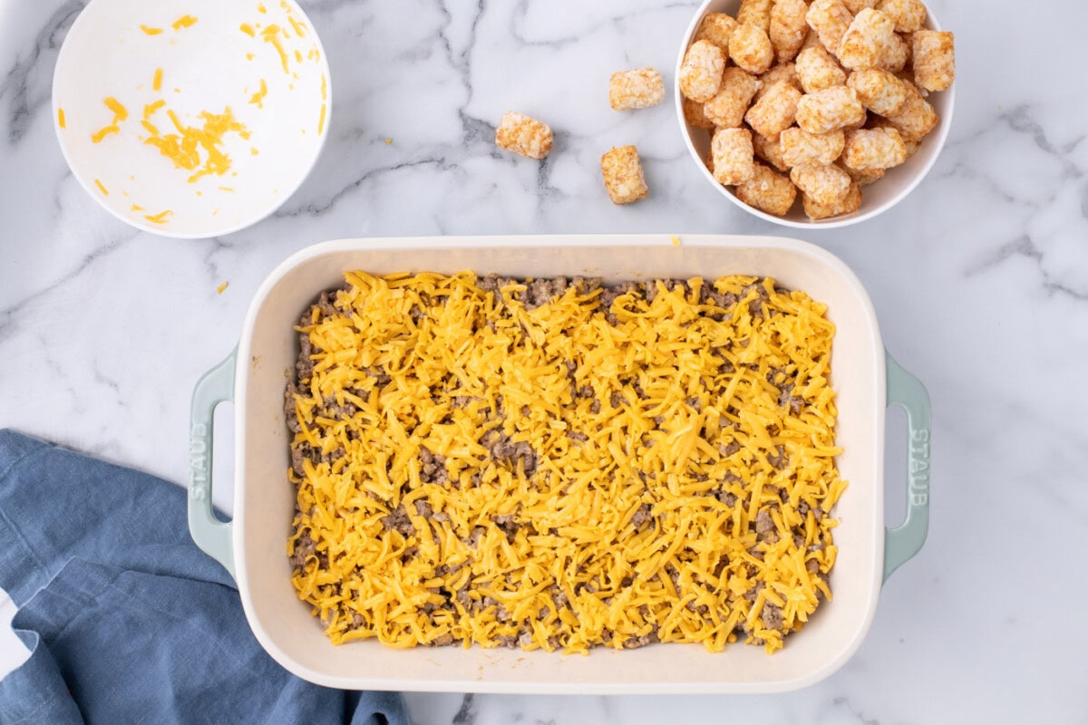 shredded cheese on top of ground beef in casserole dish